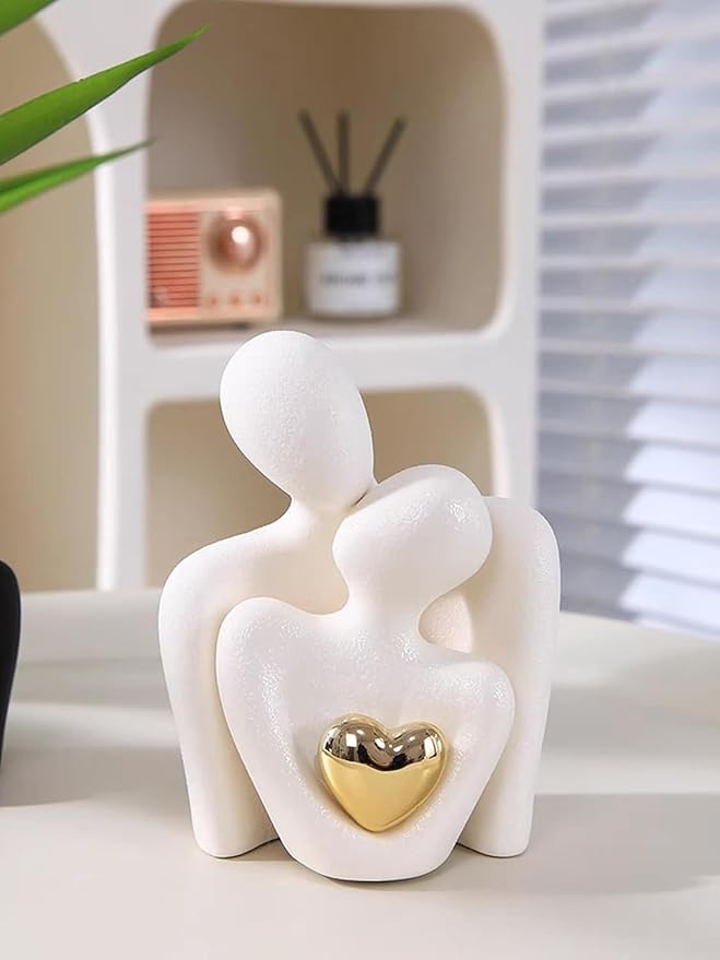 Decorative sculpture of two figures holding a heart on a shelf with a plant and decorative items in the background.
