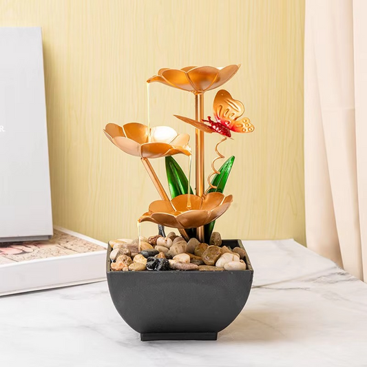 Decorative water fountain with flowers and a butterfly on a table.