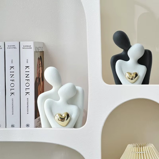 Decorative figurines of a couple with a heart on a shelf with books in the background