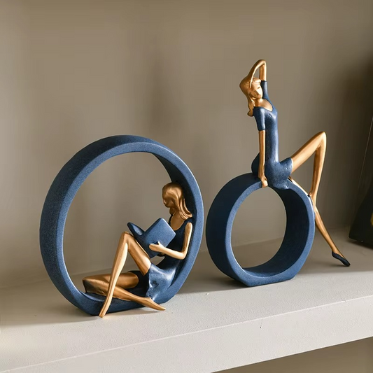 Decorative sculpture of a woman reading a book inside a blue circle with a man on top, on a neutral background.