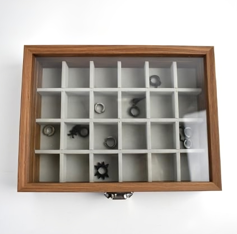 Wooden jewelry box with white interior holding various small metallic objects on a white background