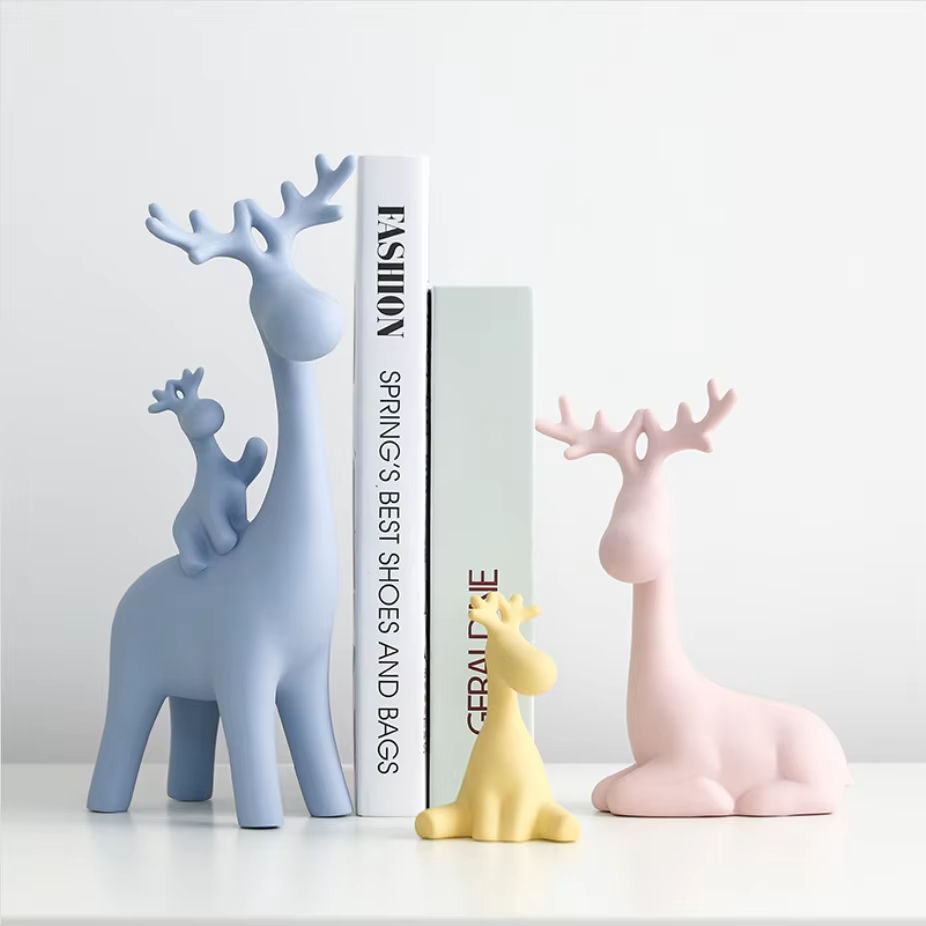 Decorative deer figurines in blue, pink, and yellow on a white surface with a magazine in the background.
