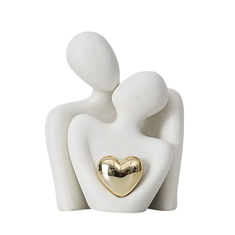 Ceramic sculpture of two figures embracing with a gold heart detail on a white background