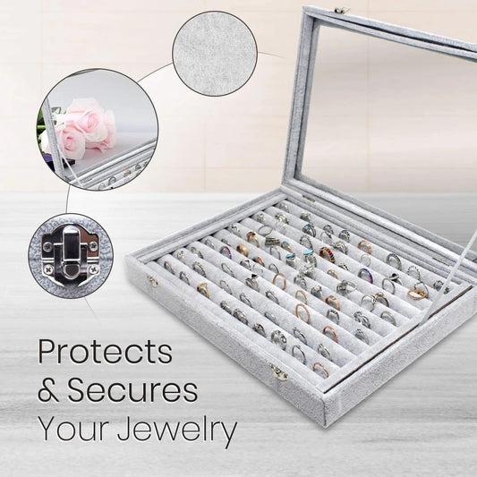 Gray jewelry display case with rings, glass lid, and velvet interior on a light background.