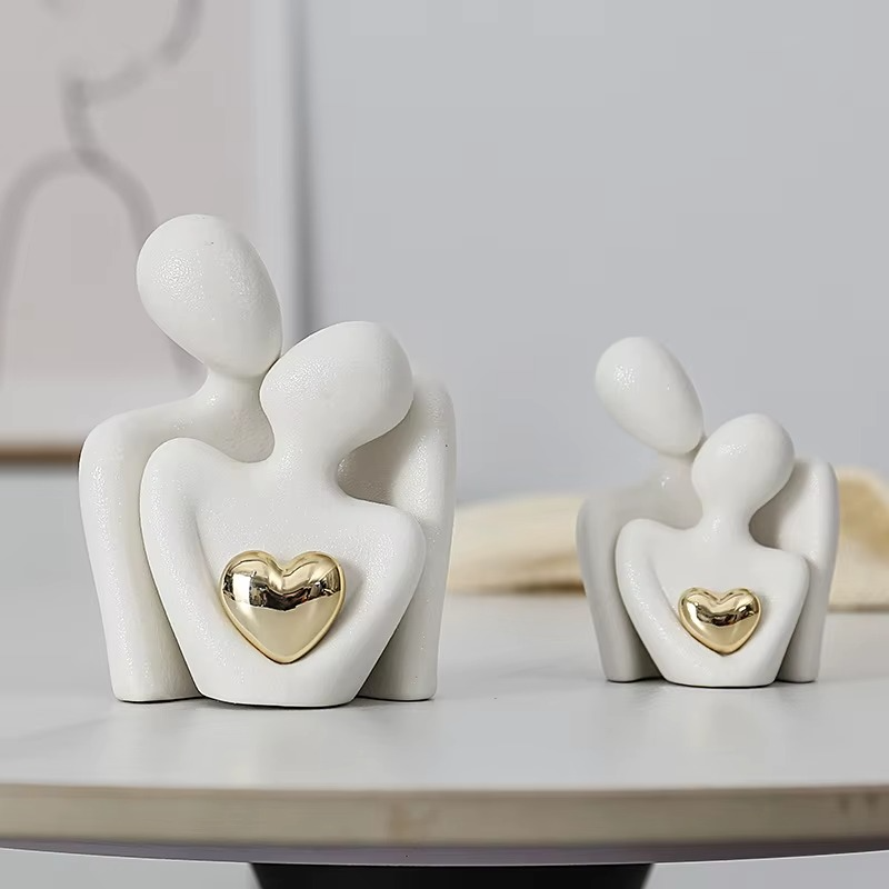 Two white ceramic figures with gold hearts on a light gray surface.