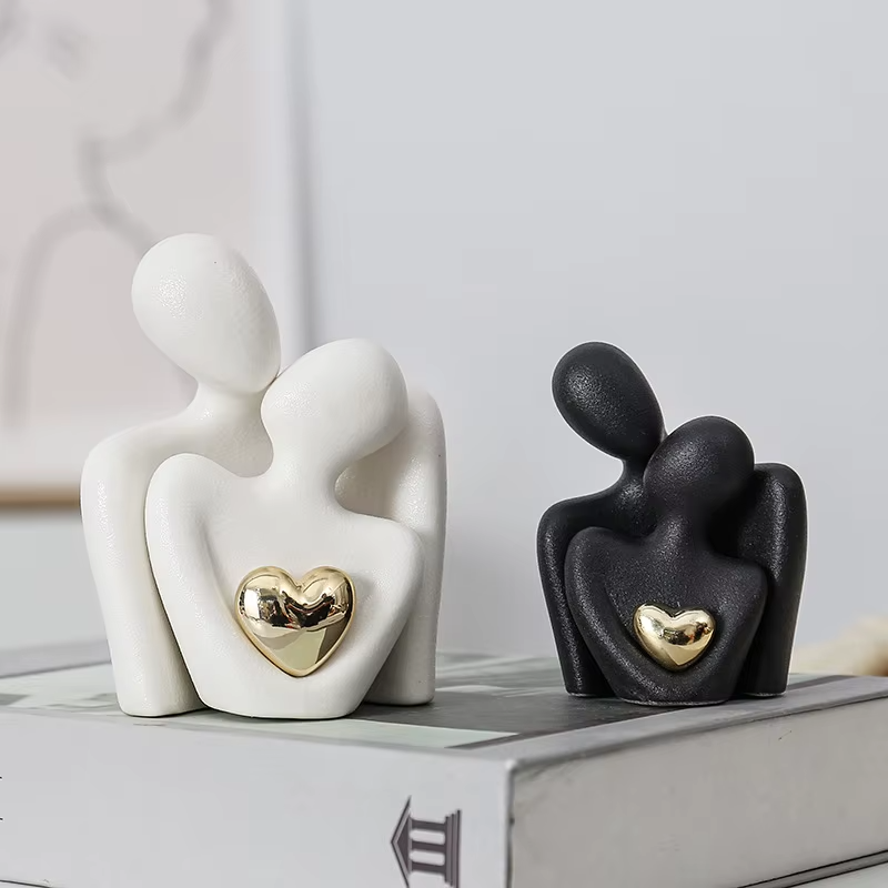 Two ceramic figures, one white with a gold heart and one black with a gold heart, on a light surface.
