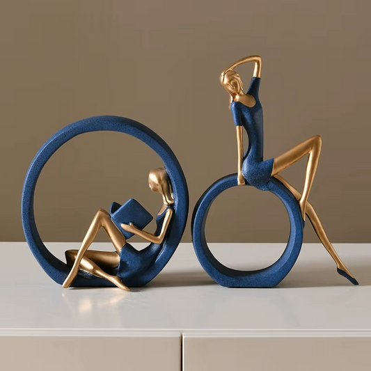 Decorative sculptures of a person reading a book and a person on a bicycle against a beige background