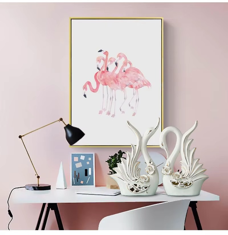 Decorative swan statues on a table with a pink wall and flamingo artwork.