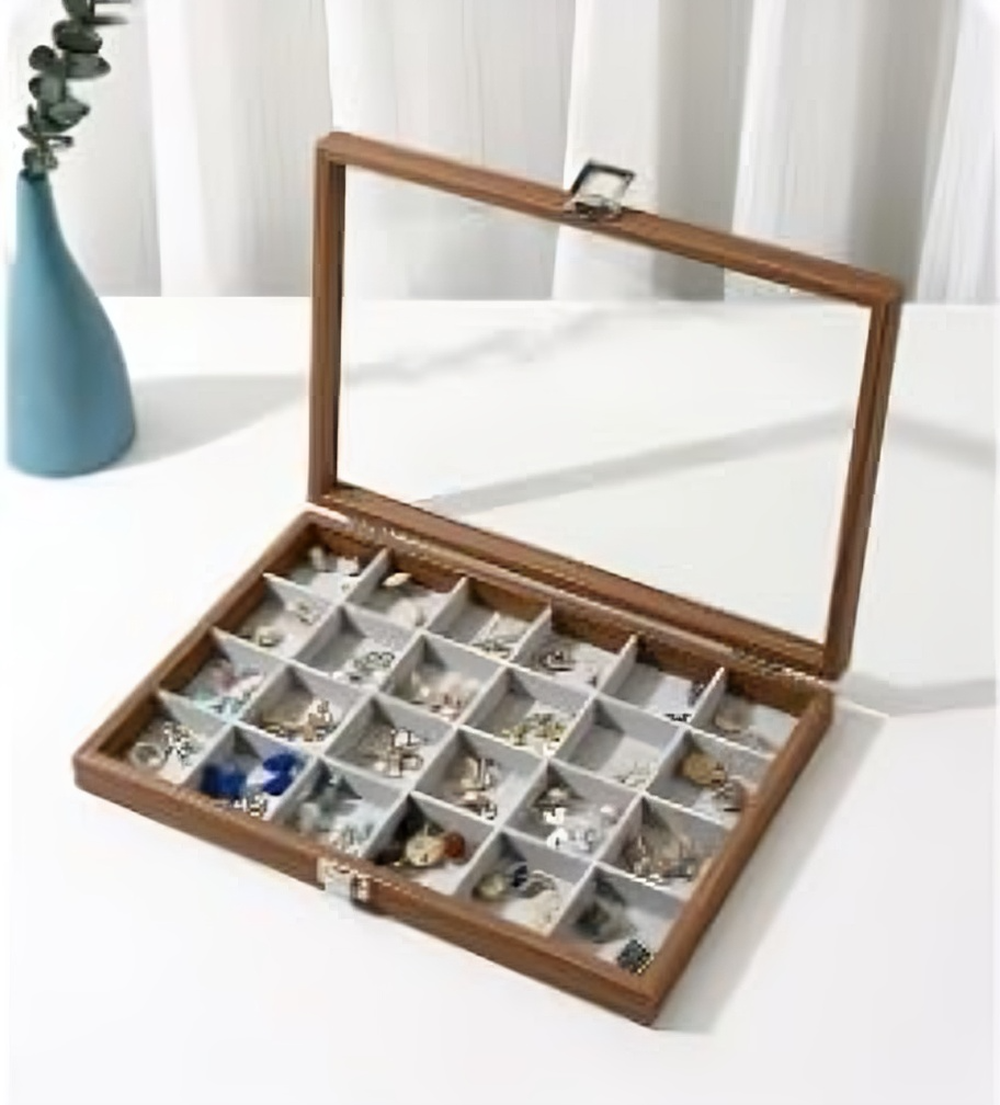 Wooden jewelry box with glass lid containing various earrings on a white surface.